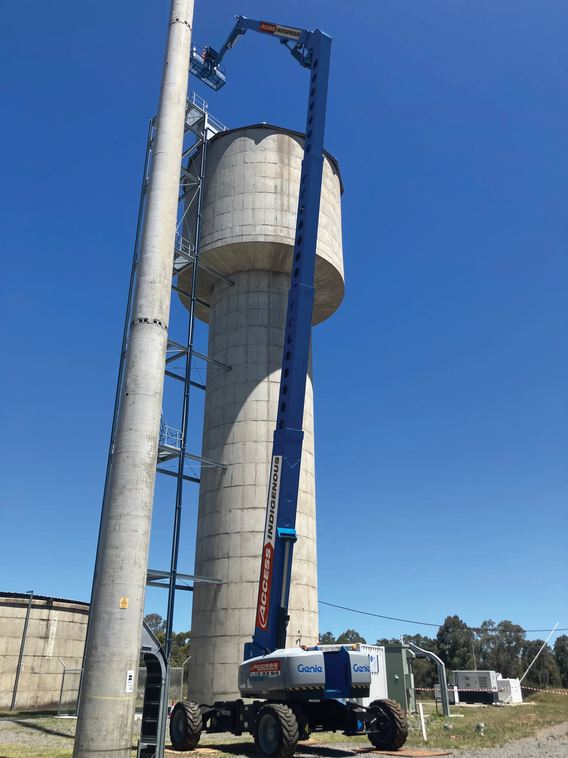 Telescopic boom lift positioned beside tall industrial silo structure